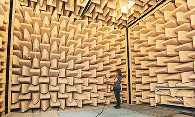 En kvinna står med ett ljudinstrument i ett rum med väggar klädda i ljudabsorberande material.