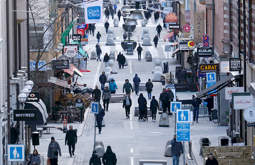 Människor promenerar längs affärsgata i stadsmiljö.
