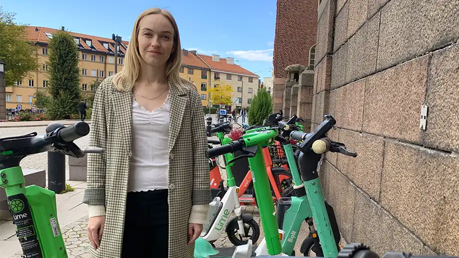 Kvinna står bredvid e-scooter parkering.