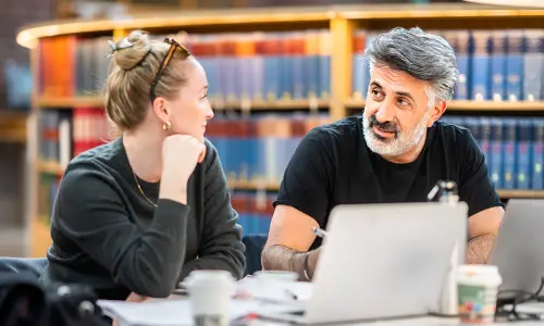 Två yrkesverksamma studenter sitter i KTH:s bibliotek och studerar.