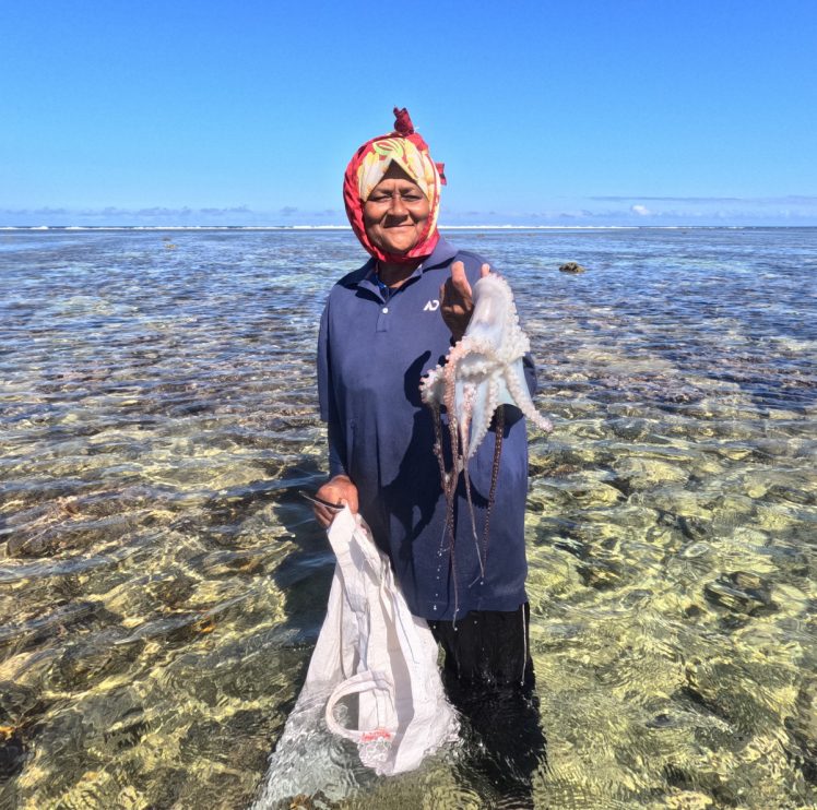 A woman standing in shallow water holds an octopus