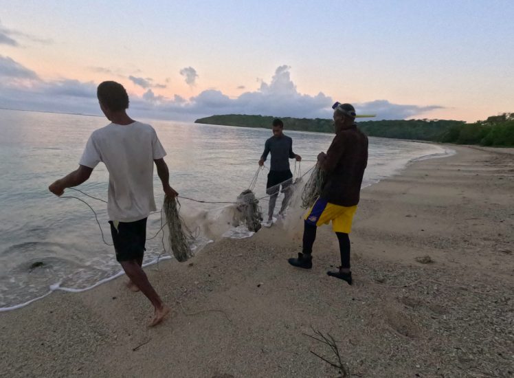 Three men on a beach holding a fishing net