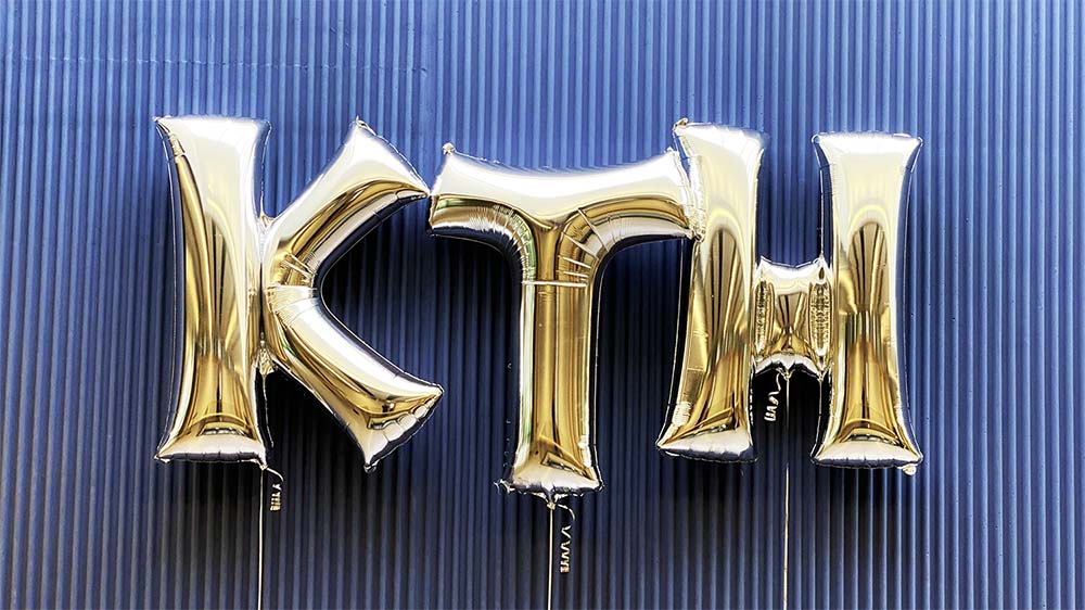 Three silver balloons spelling the word KTH against a blue wall