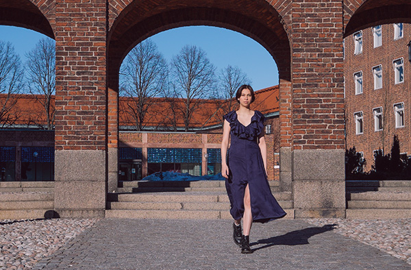 Woman in blue dress walk towards the camera. Brick buildings at KTH in the background. 