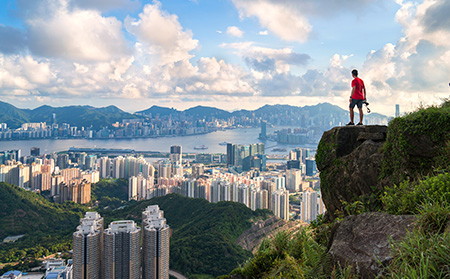 A person standing on top of a mountain overlooking a large city