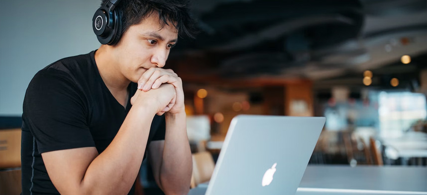 A person with headphones on, looking at a laptop while looking focused