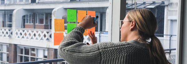 A person writing on sticky notes stuck on a big window