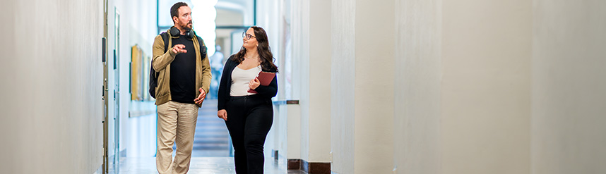 Two persons walking in a corridor, talking to eachother