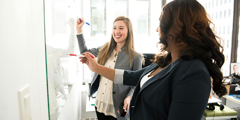 Two persons standing in front of a whiteboard with pens in their hands