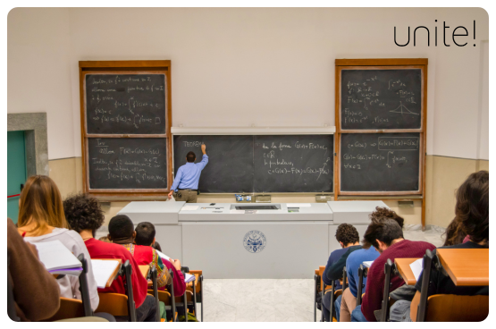 Teacher by a blackboard in a large classroom