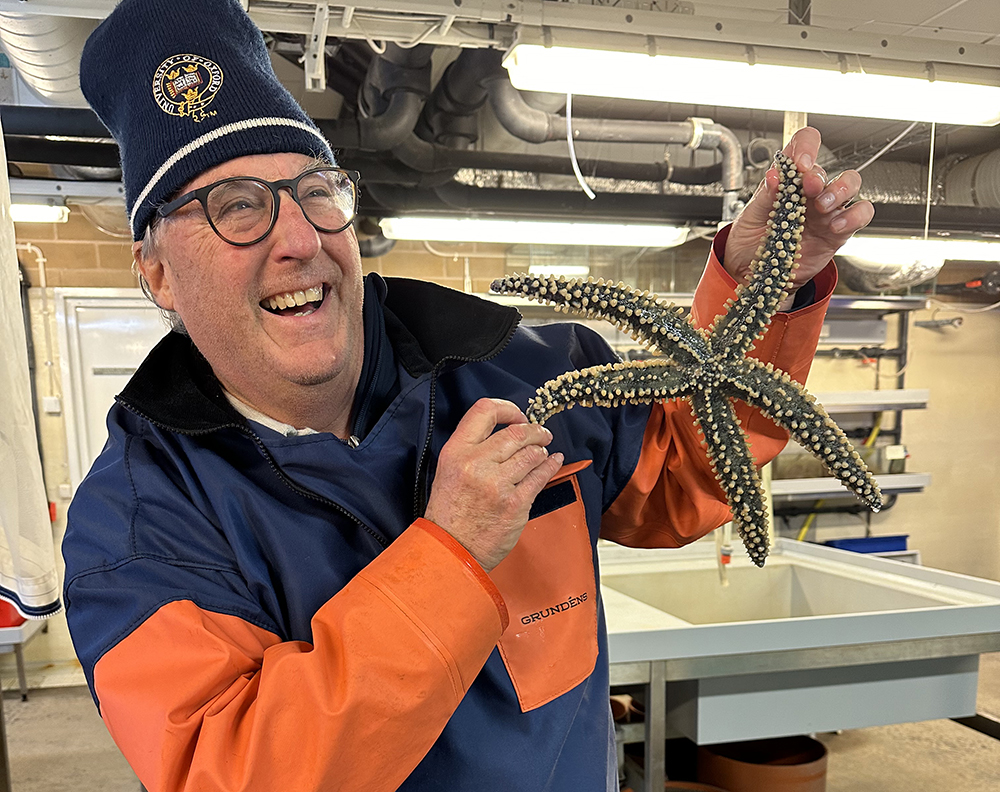 Man dressed in boating clothes holds up a starfish