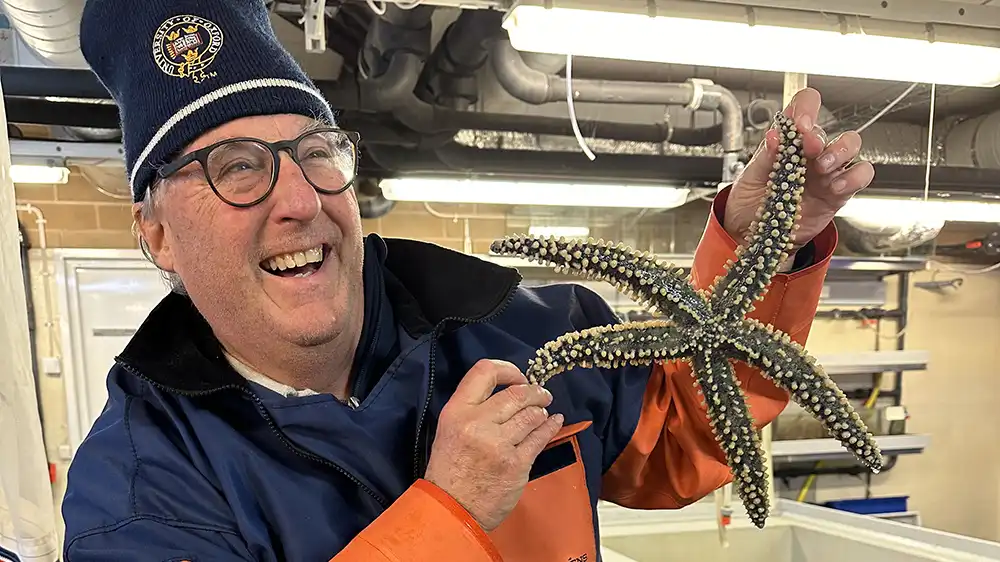 Man dressed in boating clothes holds up a starfish