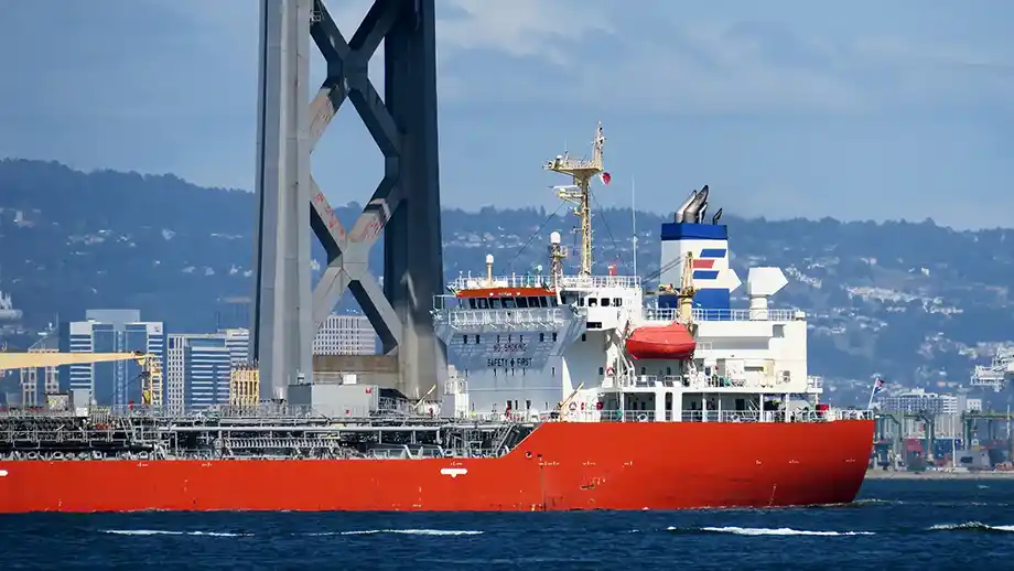 A cargo ship passes beneath the San Francisco Bay Bridge on a sunny day. 