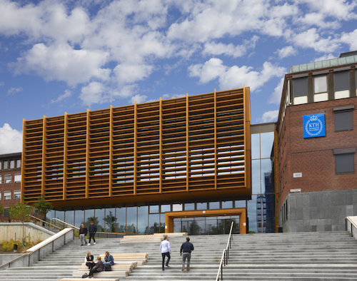 Front of KTH's building in Södertälje. Wide stairs leading up to the main entrance. KTH logotype on the wall. Blue sky with small white clouds.